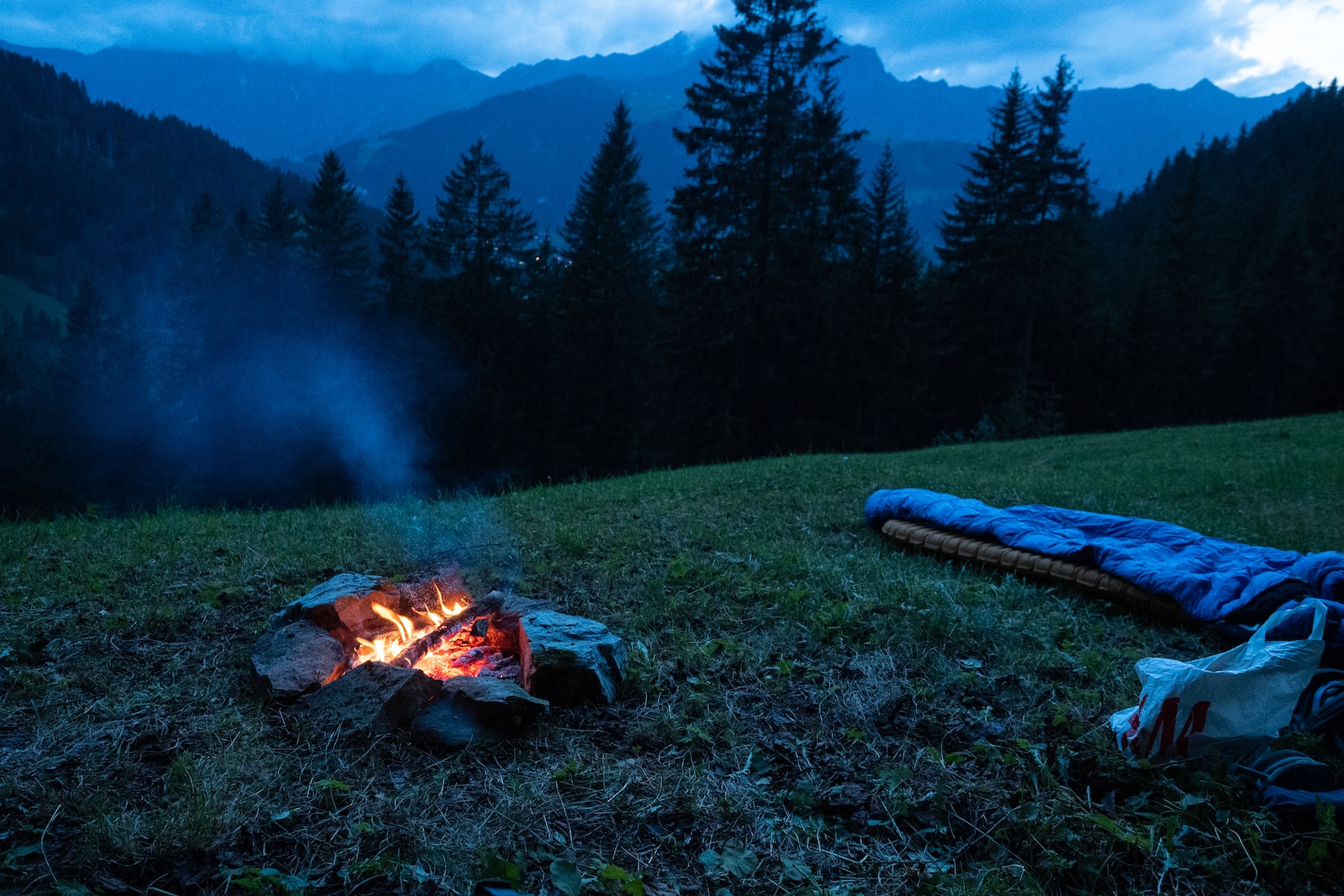 Photo by Frank Holleman bonfire on green grass field near blue tent and green pine trees during daytime